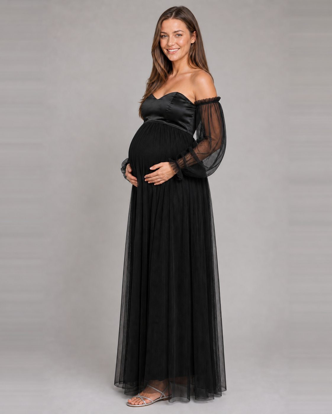 Three-quarter view of the black gown showing its raised waist, sheer long sleeves and pleated skirt.