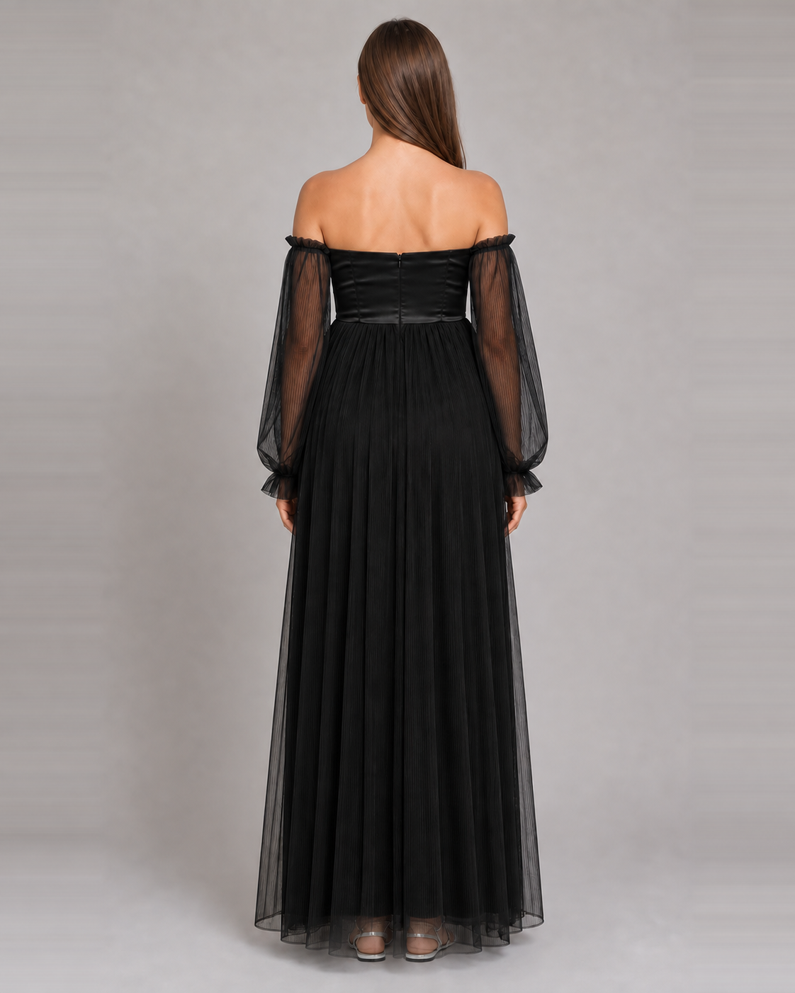 Back view of the black gown with paneled bodice seams, a center-back closure and sheer sleeves.