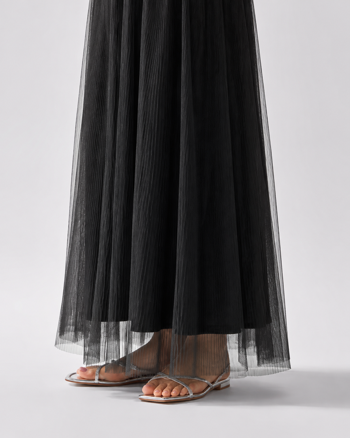 Black hem detail showing the longer sheer pleated overlay and shorter lining above silver sandals.