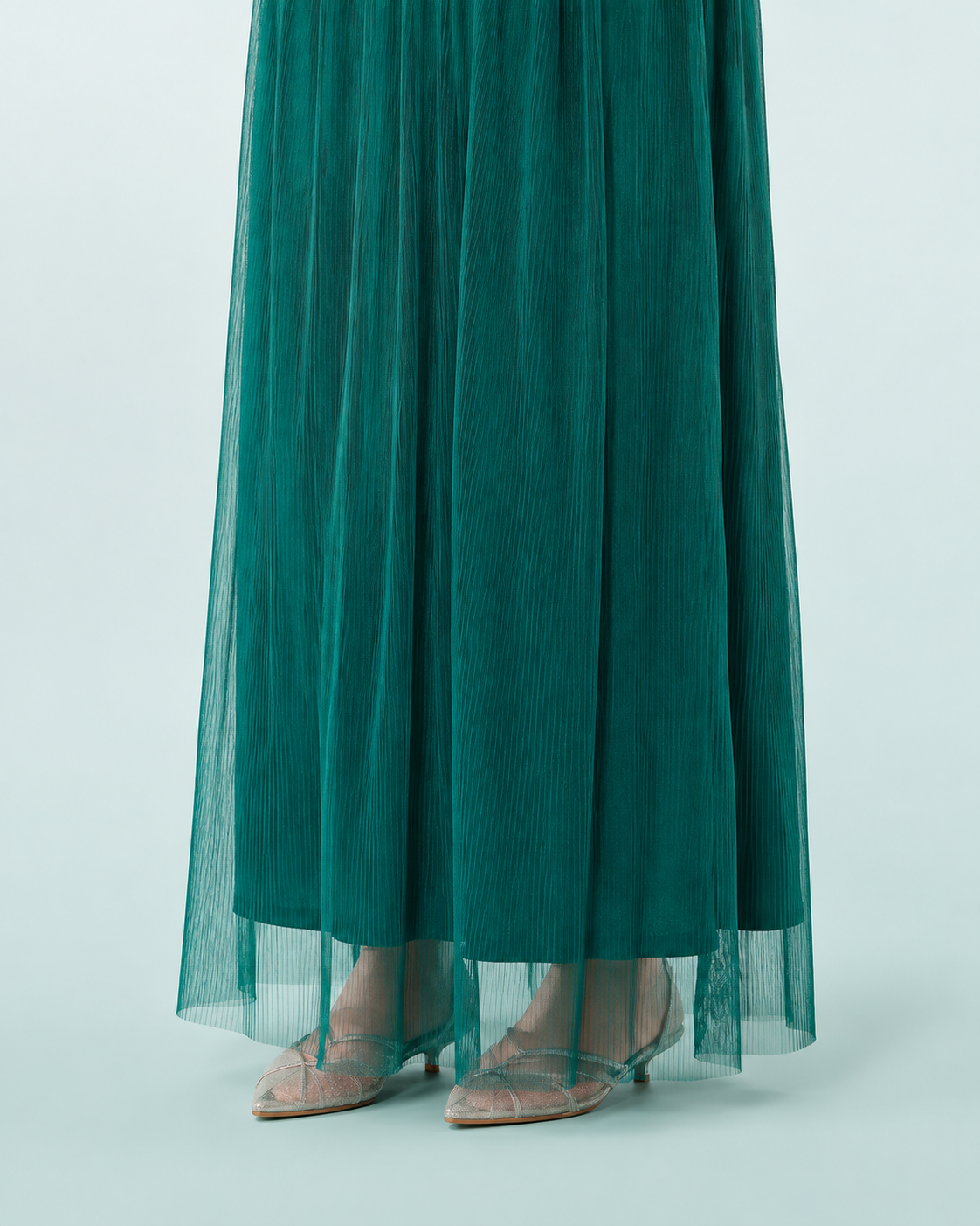 Deep green hem close-up showing the shorter lining beneath the sheer vertically pleated outer skirt.