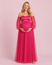 Front view of the fuchsia maternity gown with a sweetheart neckline, sheer long sleeves and a pleated full-length skirt.
