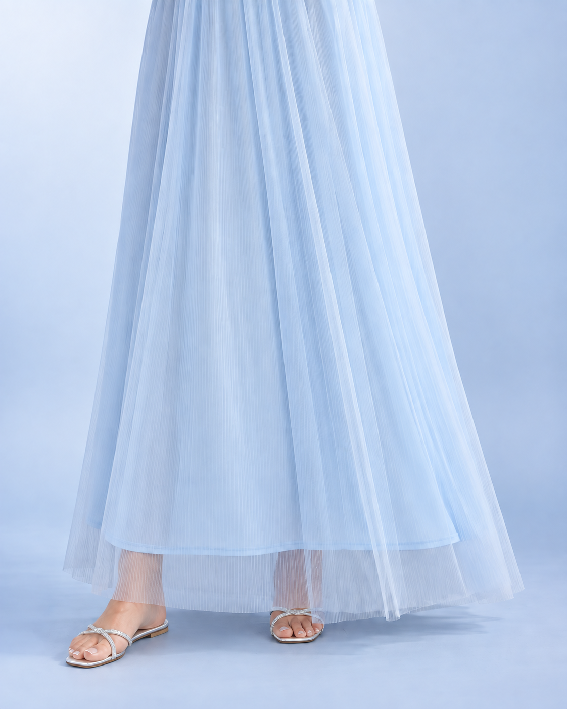 Sky blue hem detail showing the lining beneath the longer sheer pleated overlay, styled with silver sandals.