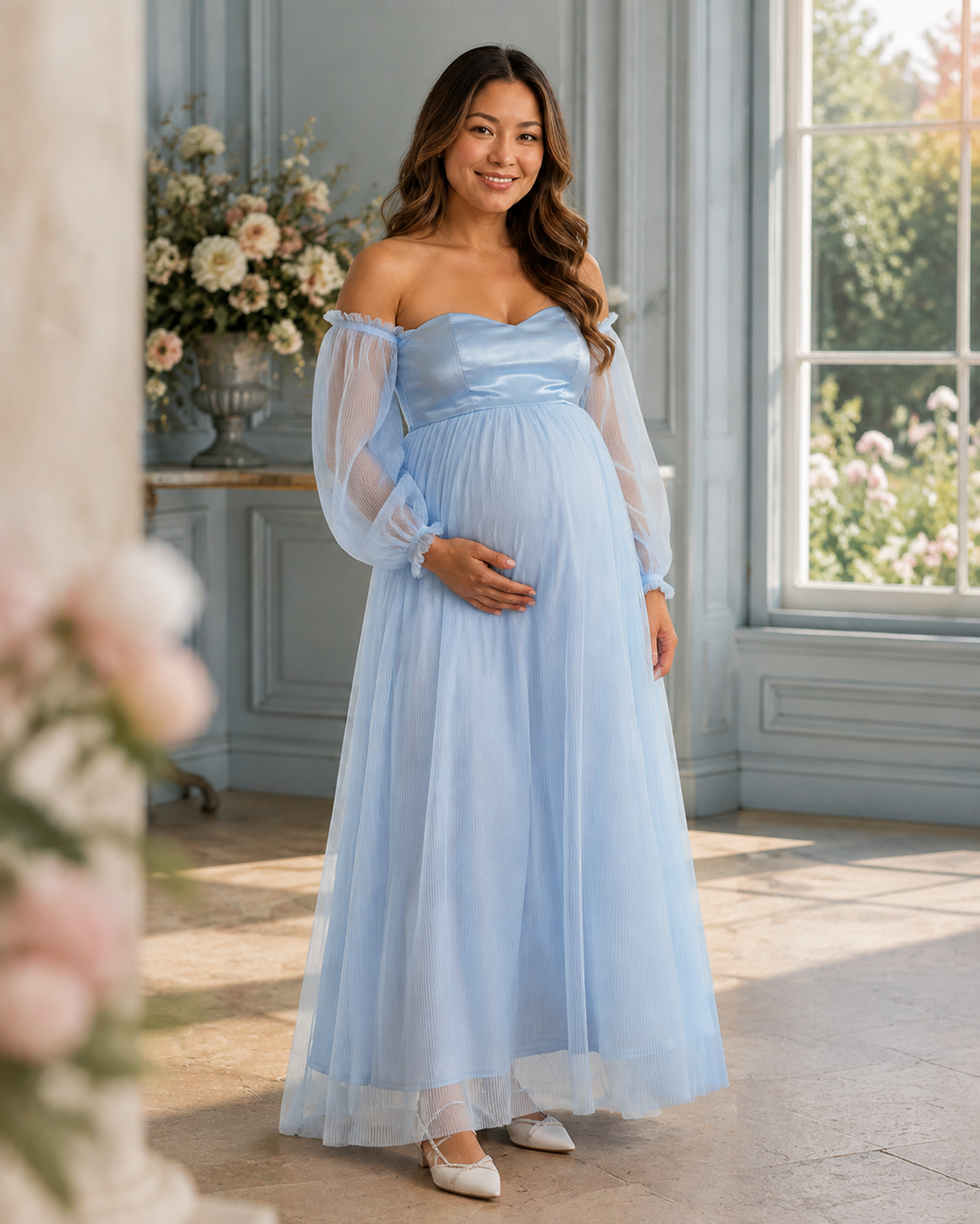 Sky blue maternity gown in a window-lit room with blue-gray walls and pale floral arrangements.