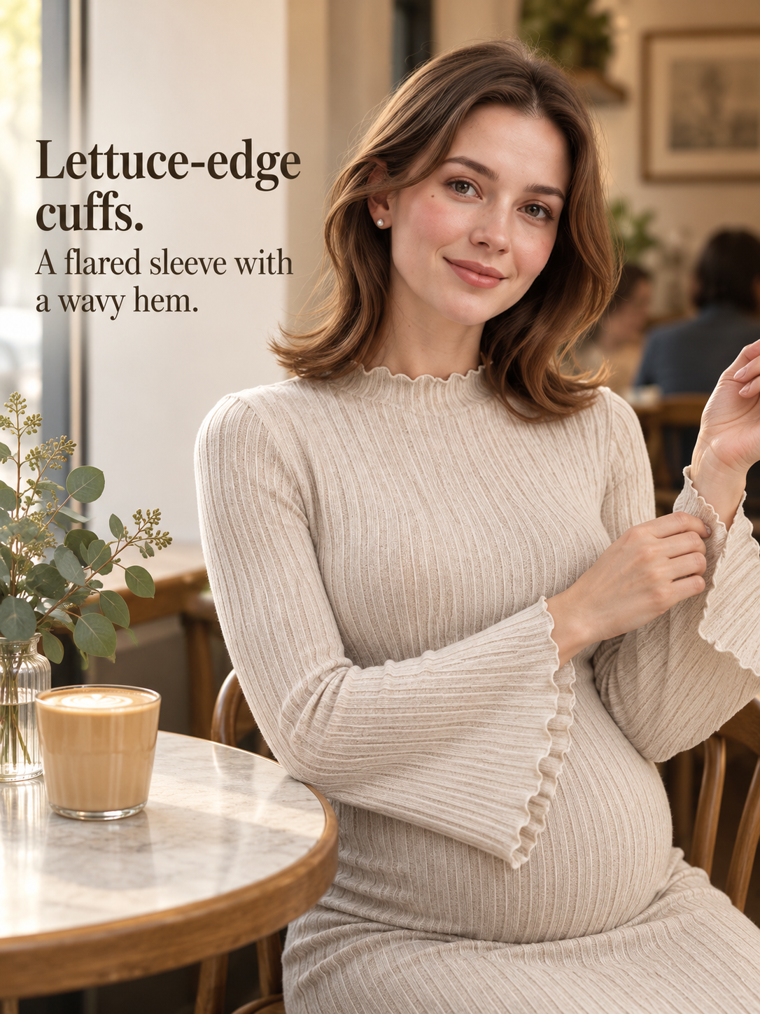 Lucienne Oatmeal maternity dress — seated at a cafe table touching the sleeve cuff