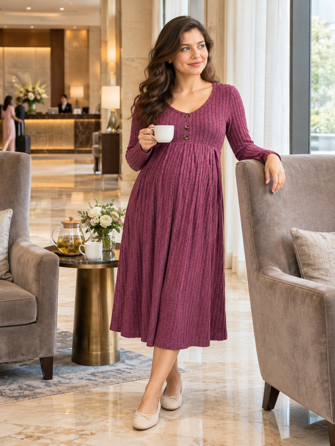 Matilda Wine Red maternity dress — standing in an elegant hotel lobby holding a teacup