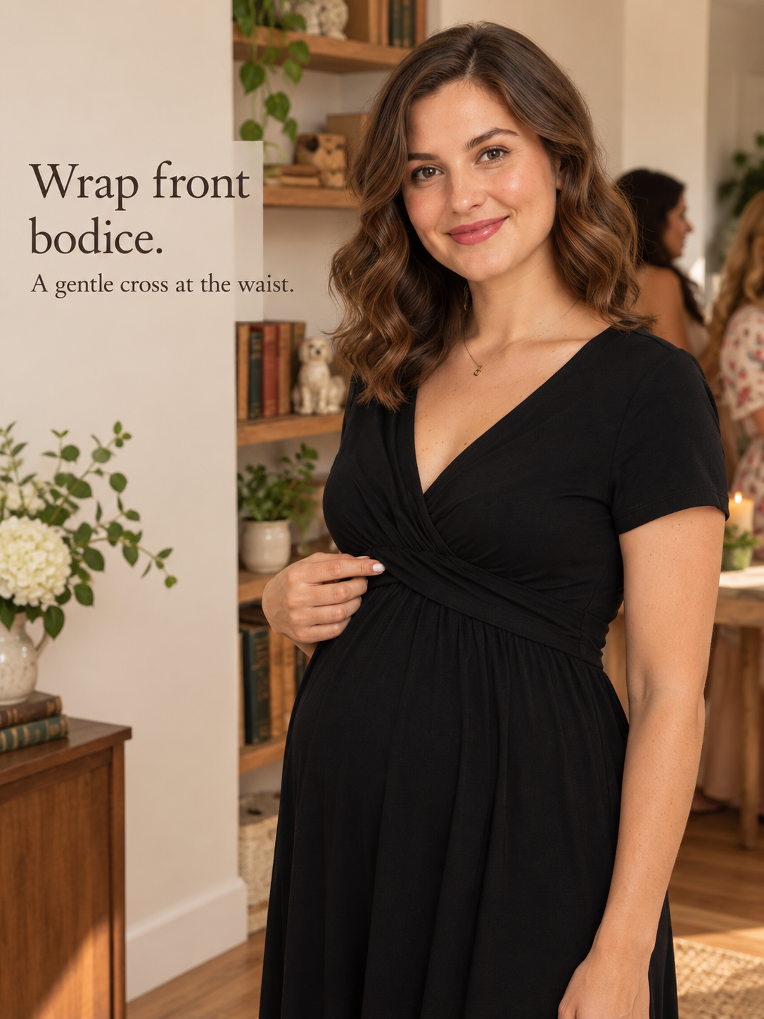 Lydia Black maternity dress — standing indoors near a bookshelf, hand at the wrap bodice