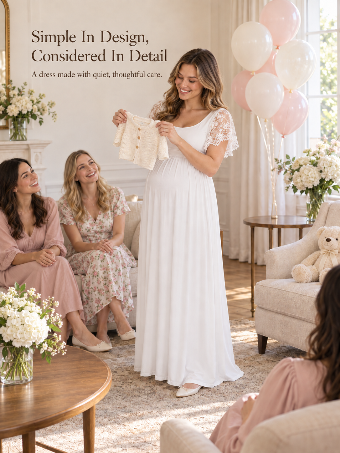 Linnea White maternity dress — holding up a tiny baby cardigan among friends
