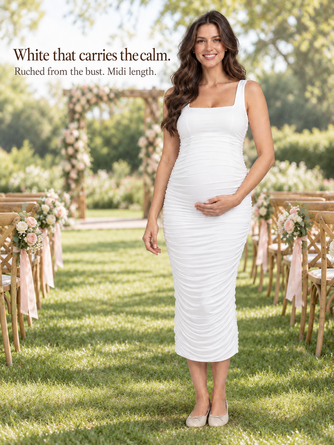 Leonie White maternity dress — standing on a garden lawn near a floral arch