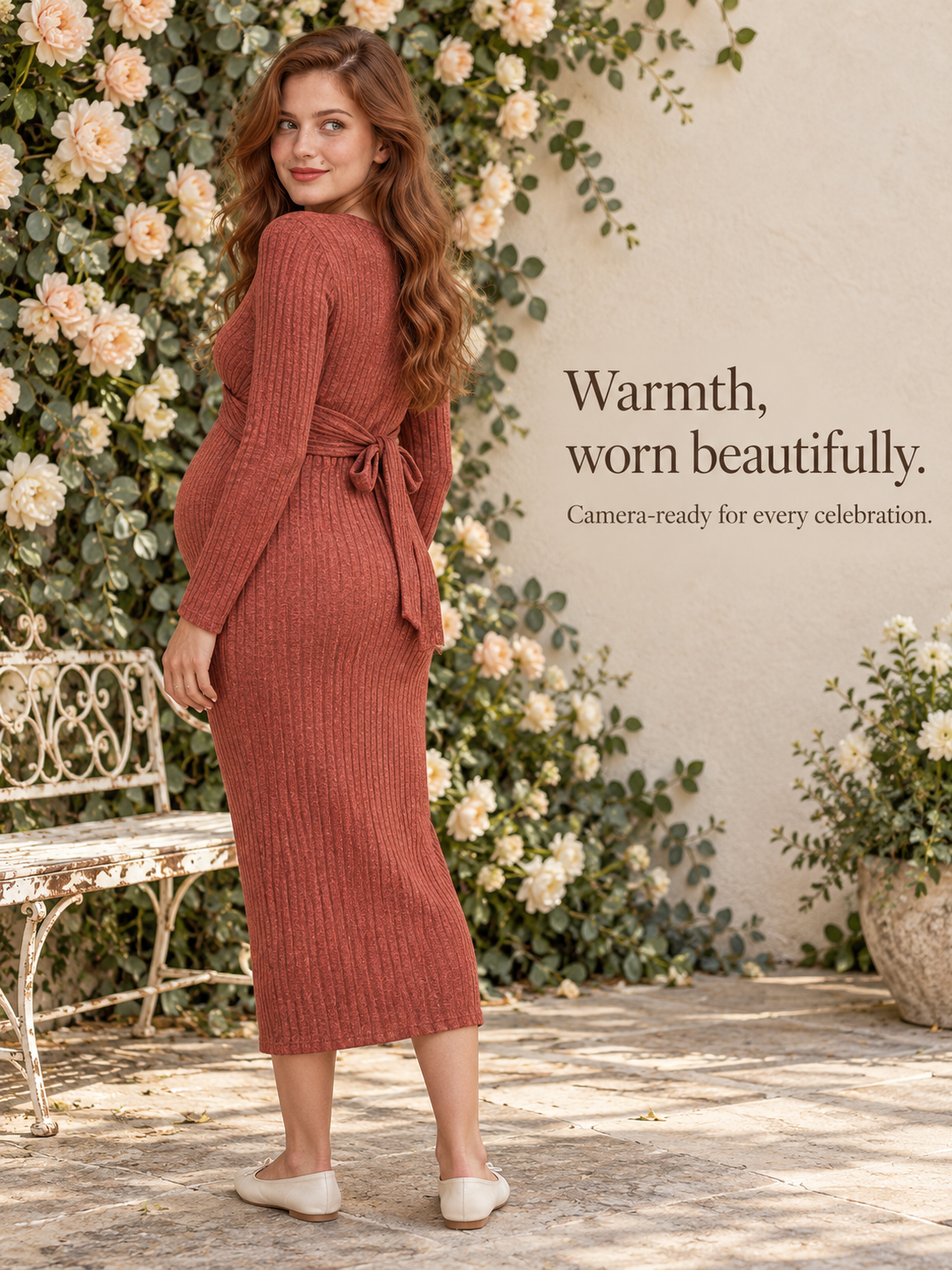 Maeve Rust Red maternity dress — walking away through a rose-covered garden wall