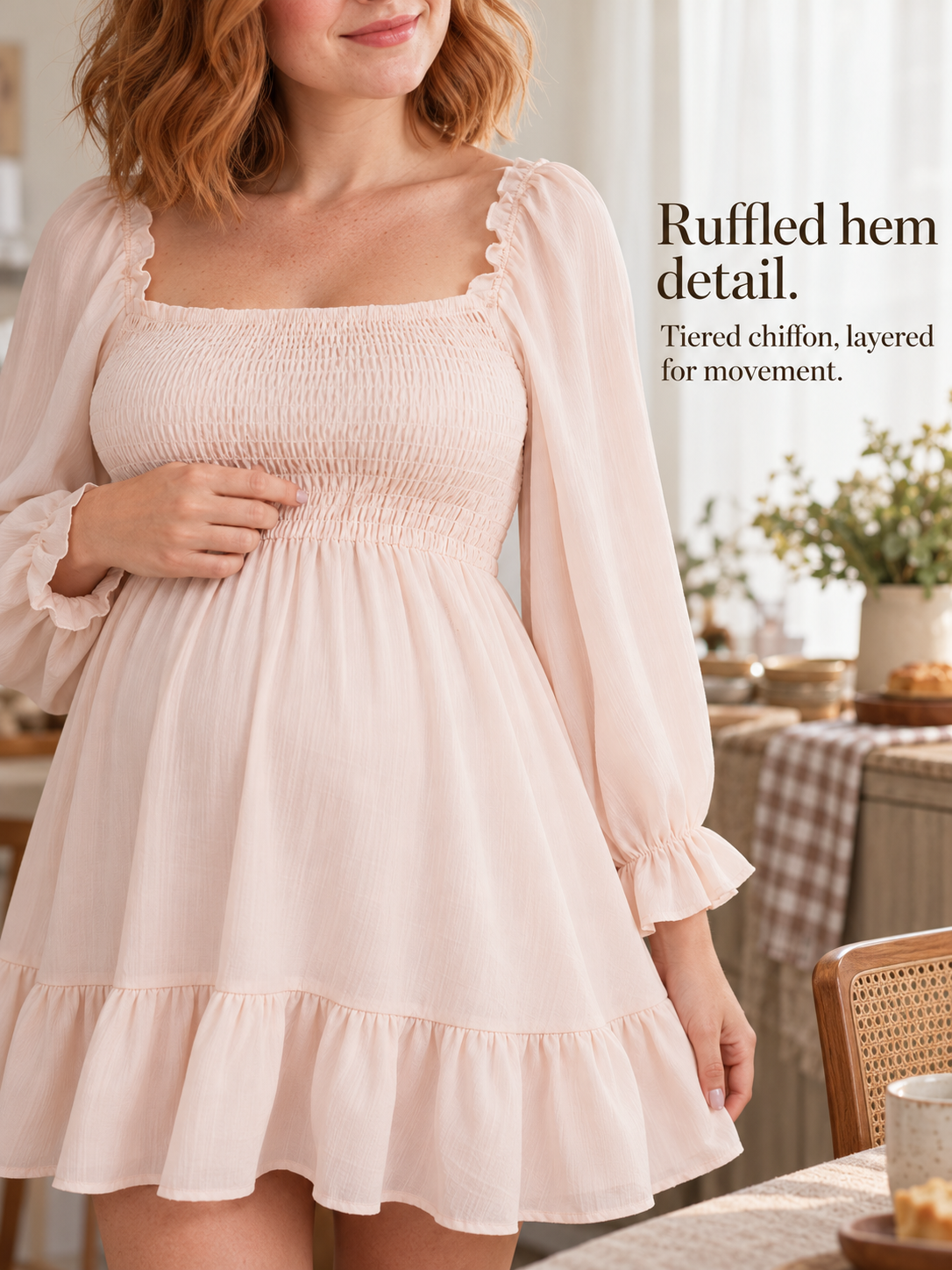 Penelope Pale Blush maternity dress — standing in a cozy living room touching the ruffled sleeve