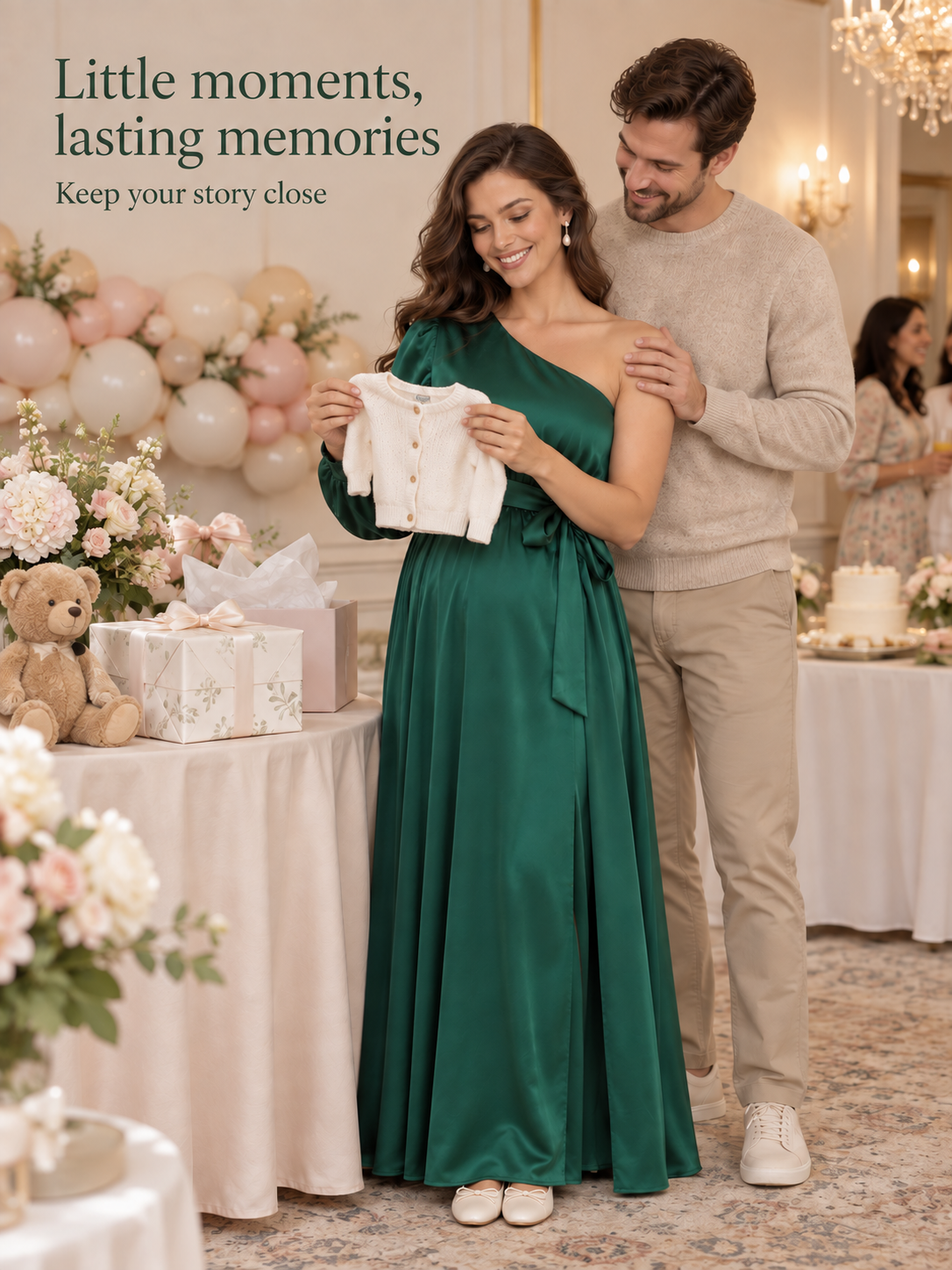 Sylvie Emerald Green maternity dress — holding a tiny baby cardigan with her partner