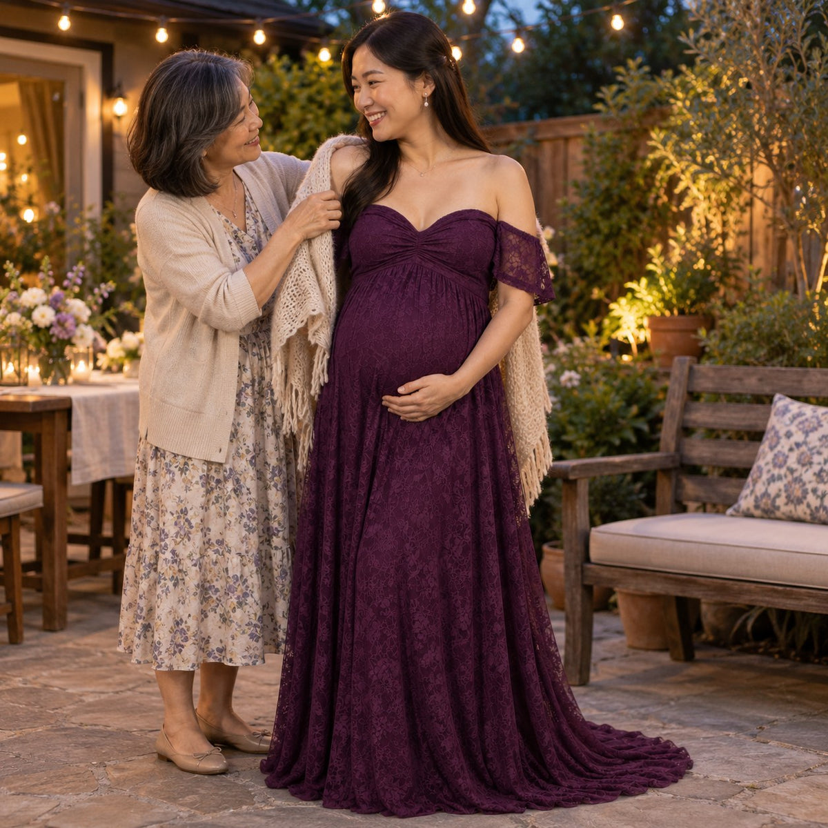 Mom-to-be in a deep plum lace maternity dress as her mother wraps a knitted shawl around her at dusk