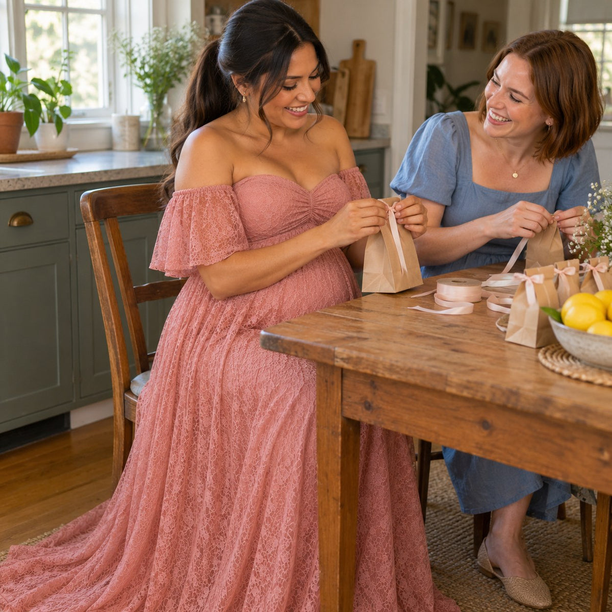 Mom-to-be in a dusty rose lace maternity dress tying ribbons on baby shower favor bags with her best friend