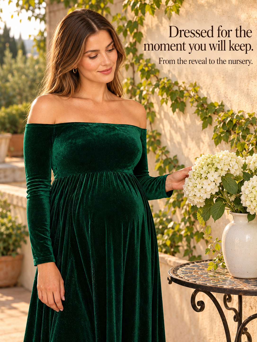 Colette Forest Green maternity dress — touching white hydrangeas on a garden terrace